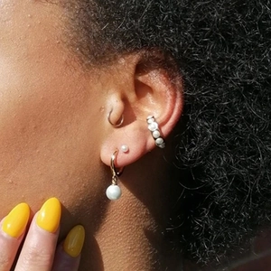Detail of gold pearl earring set including studs and ear cuff shown on model