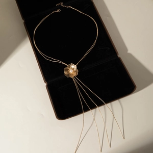 Détail du collier feuille de ginkgo doré avec perle blanche et franges métalliques