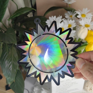 Close-up of a sun-shaped holographic suncatcher with a black frame held against garden plants
