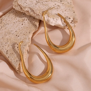Close-up of golden hollow curved earrings on beige rock and champagne silk fabric