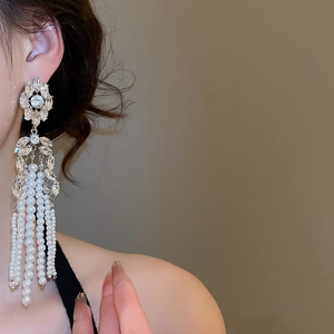 Close-up of pearl tassel earrings with crystal flower stud on model in warm lighting