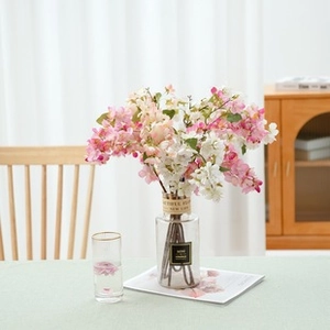 Pink and white faux cherry blossom bouquet in a glass vase on a rustic green tablecloth