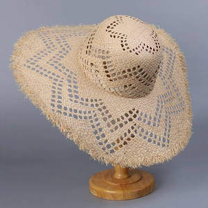 Detail of hand-woven raffia sun hat showing hollow pattern and frayed brim on wooden stand