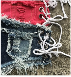 Dettagli di pantaloncini in denim strappati con occhielli in metallo e lacci