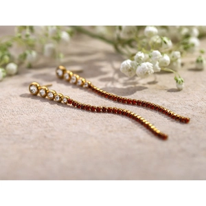 Macro shot of 18k gold earrings with long red rhinestone tassels and clear zircons