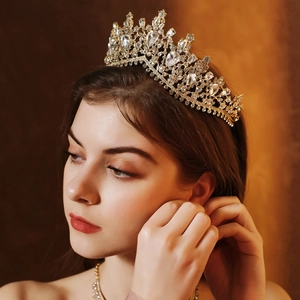 Detail of a golden bridal jewelry set featuring a crown and earrings worn by a model