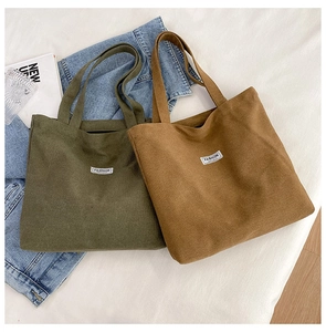 Flat lay of green and brown canvas tote bags with FASHION label on white linen bedding
