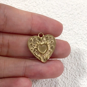 Golden heart pendant with embossed sacred heart and stars held by fingers close-up