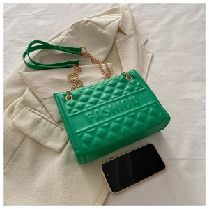 Detail of green embossed fashion bag with gold chain strap on beige blazer