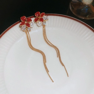 Detail of red flower tassel earrings with pearls and snake chains on a ceramic plate