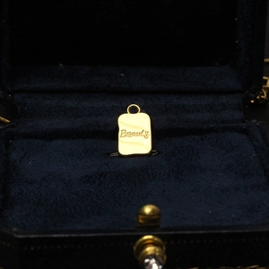Detailed close-up of a gold rectangular butterfly pendant with Beauty engraving in a gift box