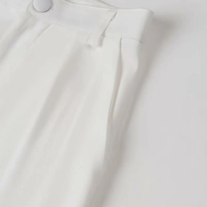 Detailed close-up of white high-waist suit trousers showing buttons and twill texture