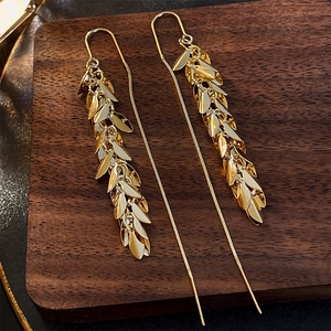 Detail of gold leaf fringe earrings showing layered wheat ear design on dark wood