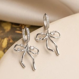 Macro shot of silver bow earrings with sparkling cubic zirconia on a warm fabric background