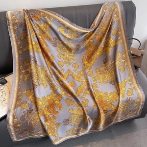 Carré de soie style baroque gris et doré présenté élégamment sur un canapé