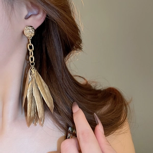 Detail of long gold feather tassel earrings on a model showing the elegant drop length