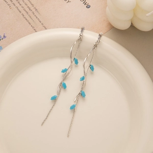 Detail of silver long tassel leaf earrings with sky blue beads on a ceramic tray