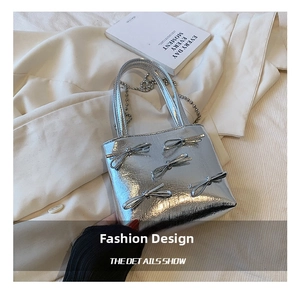 Detail of silver mirror handbag featuring textured bows and a metallic beaded chain