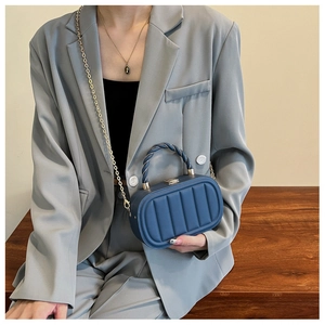 Detail of navy blue box bag with quilted pattern, golden chain and metallic lock clasp