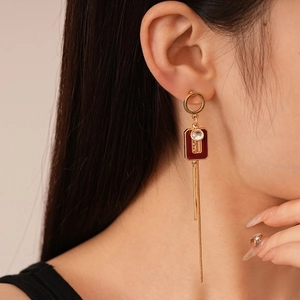 Close-up of gold geometric tassel earring with red acrylic pendant and clear crystal