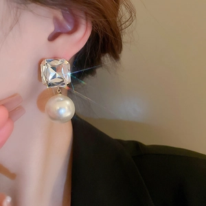 Close-up of a model wearing square crystal and round pearl drop earrings in gold finish