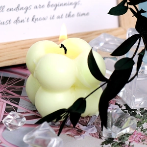Close-up of a lit yellow bubble cube scented candle with minimalist home decor props