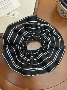 Macro detail of high-elasticity black and white striped satin scrunchie on wooden desk