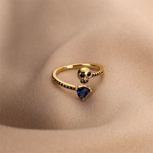 Detail of gold skull ring featuring a blue heart gemstone on pleated beige silk