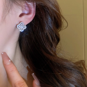 Close-up of a silver clover stud earring with sparkling rhinestones worn by a model