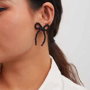 Close-up of black beaded bow earrings featuring a ribbon design on a female model