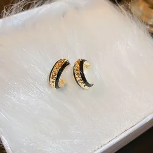 Detail of C-shaped earrings with hammered gold finish and smooth black enamel surface