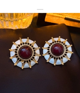 Macro shot of vintage round gold earrings with deep red gemstones and white enamel details
