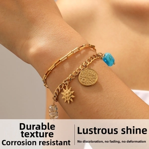Detail of layered gold stainless steel bracelets with sun pendant and blue gemstone charms