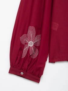 Detail of wine red cotton-linen sleeve with white floral embroidery and buttoned cuff