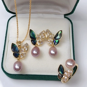 Macro shot of butterfly jewelry set with purple pearls in a dark green velvet gift box