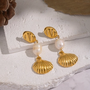 Detail of shell-shaped pearl earrings on a warm stone background with gold plating