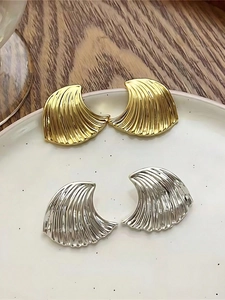 Detailed view of wave-textured earrings in gold and silver on a white ceramic tray