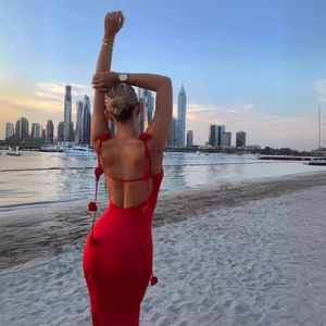 Close-up of red backless maxi dress with delicate pom-pom details on beach at sunset