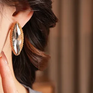 Elegant gold marquise-cut crystal stud earrings with beaded frame worn by model