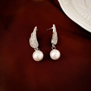 Macro detail of silver angel wing earrings with crystal pavé and glossy white round pearl