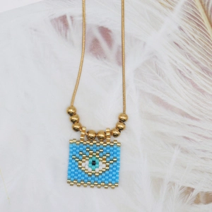 Detail of bohemian evil eye pendant with blue beads on golden snake chain and feather