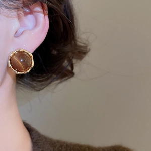 Close-up of 18k gold plated round tiger eye stone stud earring worn by a model
