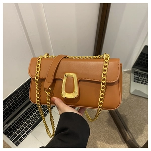 Detail showing brown leather bag with chunky gold chain strap and geometric metal buckle