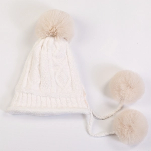 Detail view of white knit hat featuring large faux fur pom-pom and braided hanging cords