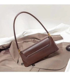 Brown leather baguette shoulder bag detail showing minimalist design and gold hardware.