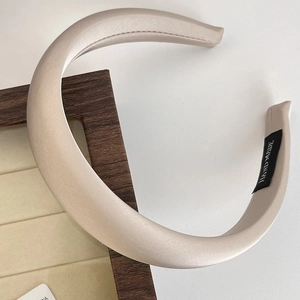 Detail of handmade wide beige satin headband with black label and soft natural lighting