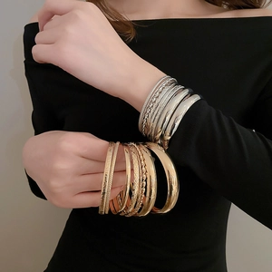 Détail de bracelets métalliques superposés dorés et argentés portés par un mannequin
