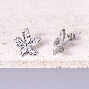 Macro detail of silver floral stud earrings featuring textured petals and butterfly back