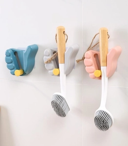 Three creative hand-shaped adhesive wall hooks holding cleaning brushes on white tile