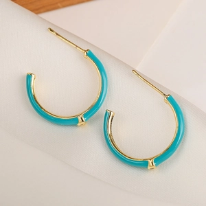 Detail of C-shaped golden hoop earrings with turquoise enamel on white silk background
